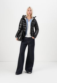 Svart boblejakke med hette, kombinert med en lyseblå skjorte og hvit topp. Bredbente mørk denim jeans og en svart håndveske.