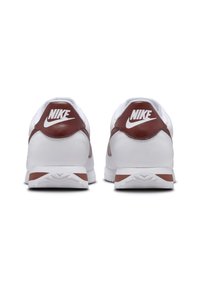Nike sneakers with a white leather body, brown accents on the heel and side, and a textured rubber sole. Features a logo on the heel.