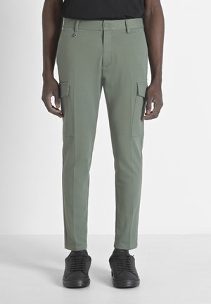 Los pantalones cargo verdes presentan un ajuste slim, tejido ligero, bolsillos laterales, una cremallera con cierre de botón y se combinan con zapatillas negras.