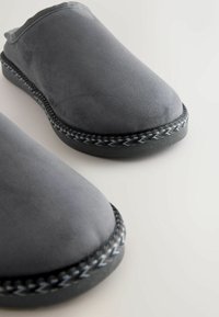 Szare zamszowe buty wsuwane z okrągłym noskiem i plecionym czarno-szarym przeszyciem wzdłuż zewnętrznej krawędzi. Płaska, teksturowana podeszwa z gumy.