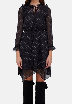 Sort gennemsigtig kjole med flæset krave og lange ærmer. Pyntet med små lyserøde prikker og bindebånd i taljen. Asymmetrisk nederkant.