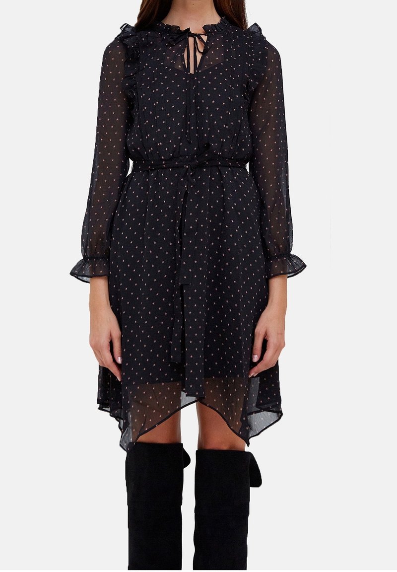 Robe noire transparente avec col à volants et manches longues. Parsemée de petits pois roses et dotée d'une ceinture à nouer à la taille. Ourlet asymétrique.
