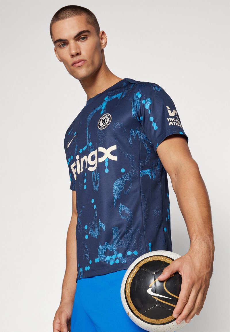 Maglietta blu e navy con motivi astratti, dotata di colletto rotondo e maniche corte. Logo sul petto; persona che tiene in mano una palla nera e oro.