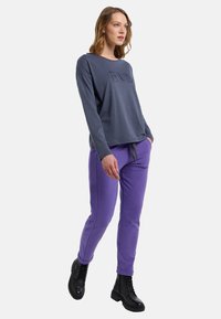 Dunkelgraues Langarmshirt mit erhabenem Aufdruck, kombiniert mit lila Jogginghosen und schwarzen Schnürstiefeln. Lockere Passform und weicher Stoff.