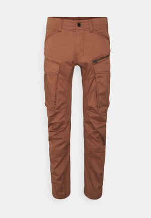 Braune Cargo-Hose in schmaler Passform mit mehreren Taschen, darunter eine mit Reißverschluss an der rechten Oberschenkelpartie, auf weißem Hintergrund dargestellt.