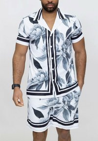 Ensemble composé d'une chemise à manches courtes avec boutons et d'un short, de couleur blanche avec un motif floral gris, des rayures noires et des détails contrastants en noir.
