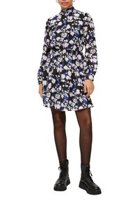 Zwarte jurk met een bloemenpatroon in paars en wit, lange mouwen, hoge kraag en een cinched taille. Gemaakt met zwarte veterschoenen.