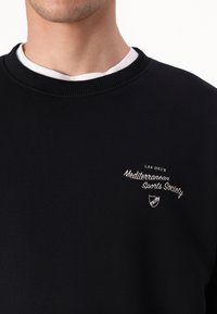 Black sweatshirt featuring ribbed collar and a white inner layer. Embroidered logo reading "Mediterranean Sports Society" on the chest.
