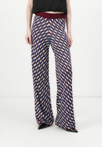 Pantaloni larghi a fantasia con forme geometriche in rosso, blu e crema. Vita elastica per il comfort, abbinati a scarpe nere a punta.