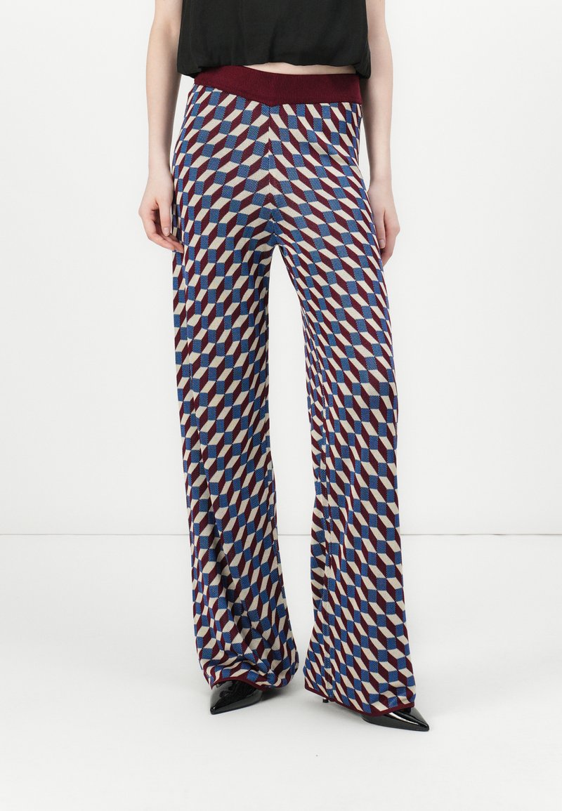 Pantaloni larghi a fantasia con forme geometriche in rosso, blu e crema. Vita elastica per il comfort, abbinati a scarpe nere a punta.
