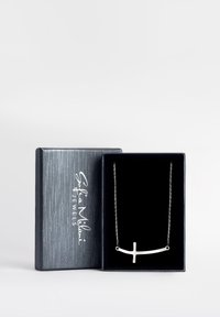 Srebrny naszyjnik w kształcie krzyża wyeksponowany w pudełku wyłożonym czarnym aksamitem. Posiada smukły design z delikatnym łańcuchem i minimalistycznymi akcentami.