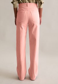 Różowe spodnie sztruksowe o szerokich nogawkach, z widocznymi tylnymi kieszeniami i fakturowaną, prążkowaną tkaniną. Dopasowany pas z szlufkami na pasek.