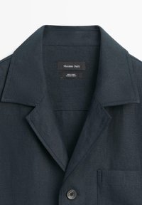 Mørk marineblå linnedjakke med brede revers, forreste knap, brystlomme og mærke med teksten "Massimo Dutti, 100 % linned, fremstillet i Tyrkiet."