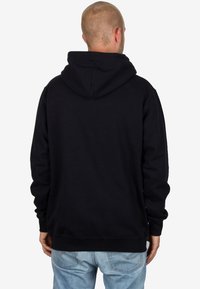 Sudadera con capucha negra de textura suave, con mangas largas y un bolsillo tipo canguro en la parte frontal, combinada con jeans de color azul claro.