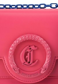 Roze leren handtas met een ronde, gevlochten roze embleem en een blauwe kettingriem. Het ontwerp toont een opvallend "Just Cavalli" logo.