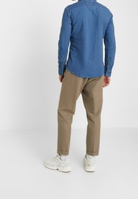 Blauw gestreepte overhemd met knopen en een gebogen zoom, gecombineerd met tan broek. Heeft lange mouwen met knoopmanchetten en witte sneakers.