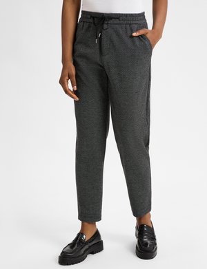 Zwart-wit gestreepte broek met een elastische tailleband en trekkoord. Tapered leg ontwerp, gecombineerd met een aansluitend wit topje en zwarte instappers.