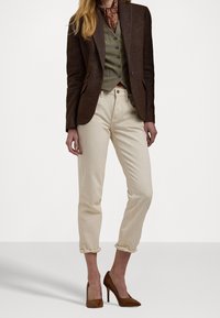 Brun texturerad blazer över en grön väst, ljusbeige rullade jeans och bruna högklackade skor. Outfiten har en accentduk.