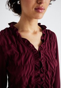 Κουμπούρντι μπλούζα με ριγμένο λαιμό και υφασμάτινη υφή. Διαθέτει διακριτικά σίγαση, μακριά μανίκια και ανοιχτό V λαιμό.