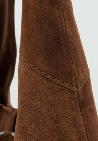 Brunt mockaskinn material med en texturerad finish. Har snygga sömmar längs kanterna och en slät, formad design.