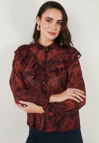 Pöttyös, redőtött galléros blúz gombos elülső résszel. Áttetsző anyag virágmintákkal. Hosszú ujjak gombos mandzsettával.