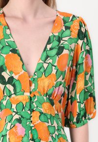 Blumenkleid mit orangefarbenen Rosen und grünen Blättern auf cremefarbigem Hintergrund. Tiefer V-Ausschnitt, kurze Puffärmel und Knopfdetails an der Taille.
