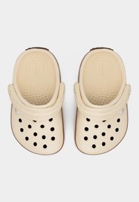 Μπεζ παπούτσια τύπου κλογκ με τρύπες αερισμού και ρυθμιζόμενα λουριά στη φτέρνα, εμφανίζονται από πάνω σε λευκό φόντο.