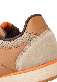 Brown and tan sneaker featuring a textured woven panel, smooth leather accents, and an orange trim on the sole. Suede texture near the heel.