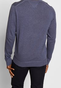 Pull en maille bleu foncé pour homme, manches longues, poignets et ourlet côtelés, avec une texture lisse et des détails subtils aux épaules.