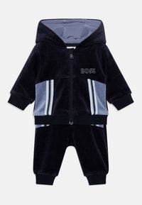 Survêtement pour bébé en bleu marine et bleu clair, avec capuche, fermeture éclair à l'avant, poignets côtelés, panneaux latéraux rayés et logo "BOSS" sur la poitrine.