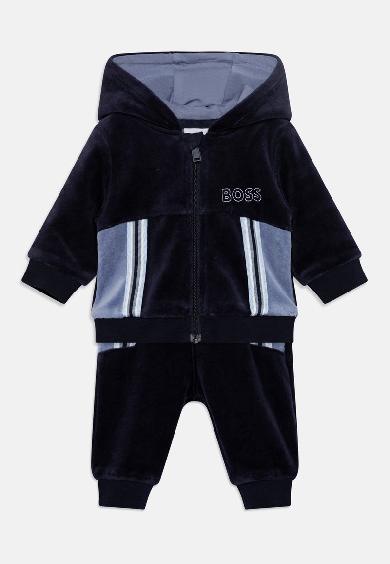 Survêtement pour bébé en bleu marine et bleu clair, avec capuche, fermeture éclair à l'avant, poignets côtelés, panneaux latéraux rayés et logo "BOSS" sur la poitrine.