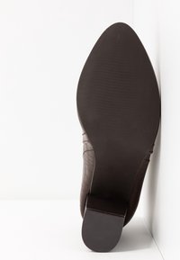 Zapato de cuero marrón con un patrón texturizado y en relieve. Presenta una suela suave y redondeada con un tacón sutil y tracción de goma estriada.