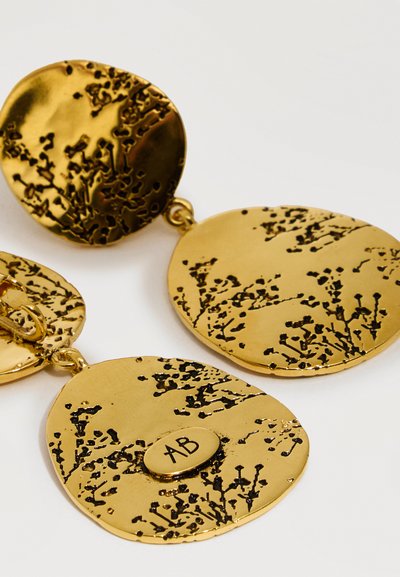 Σκουλαρίκια σε οβάλ σχήμα με επιχρύσωση, διακοσμημένα με υφασμένα μαύρα λουλουδένια μοτίβα και μια μικρή οβάλ πλακέτα με χάραξη "AB" σε κάθε κομμάτι.