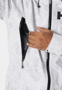 Veste blanche imperméable avec une finition texturée, dotée d'une poche zippée noire et de poignets ajustables. Conçue pour résister aux intempéries et à l'utilité.