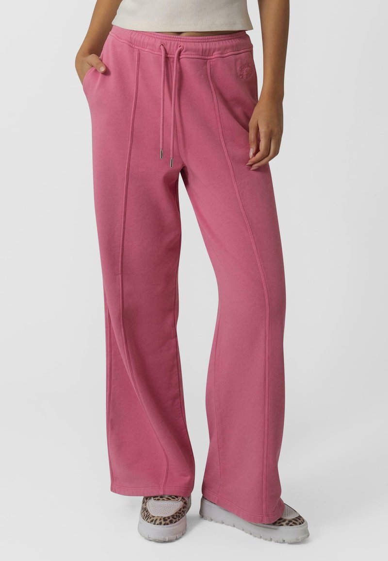 Pantalon de jogging rose avec taille à cordon, poches latérales et coupe décontractée avec des détails de couture. Associé à des baskets texturées.