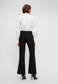 Svarta utsvängda byxor med skräddarsydda linjer och sidofickor, i kombination med en vit blus med puffärmar och rundad krage.