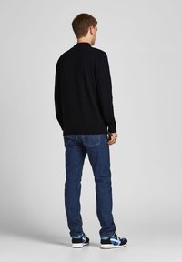 Pull en maille marine, jean bleu et baskets noires avec des accents bleus. Le pull présente un col rond et des poignets côtelés.