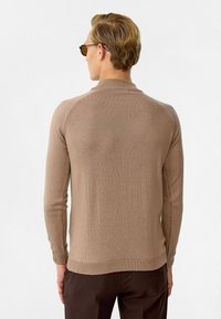 Bruine, long-sleeve trui met een hoge kraag en geribde manchetten. Gladde textuur, aansluitend ontwerp en subtiele naaddetails op de schouders.