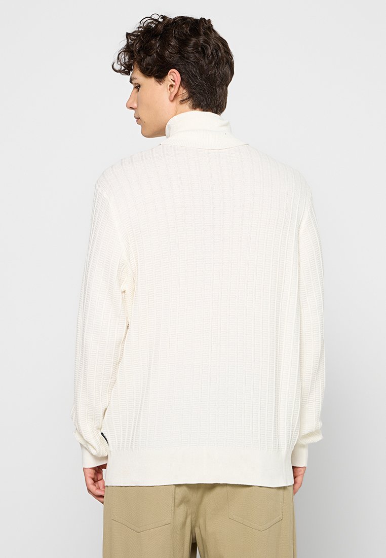Maglione lavorato a maglia color avorio con un motivo a coste textured, colletto alto e maniche lunghe, caratterizzato da una vestibilità ampia e spacchi laterali all'orlo.