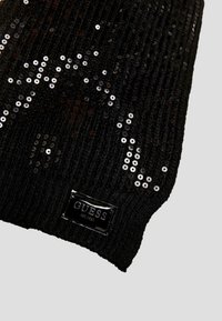 Beanie di maglia nera con texture a coste, adornato con paillettes argento e una patch lucida nera con l'etichetta "GUESS EST. 1981."