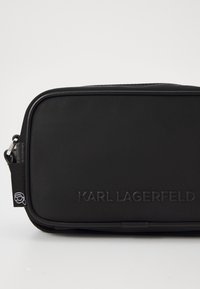 Black rectangular bag made of textured material. Features a smooth zipper and embossed "KARL LAGERFELD" logo on the front, with an icon tag.