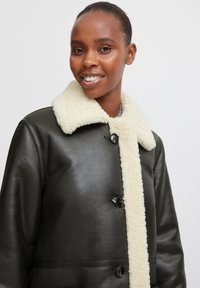 Schwarze Lederjacke mit einem cremefarbenen Lammfellkragen, mit Knopfverschlüssen und einer glatten Textur, entworfen für eine taillierte Silhouette.