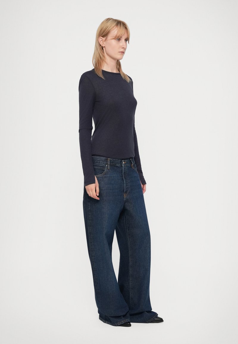 Langärmliges navy Oberteil kombiniert mit übergroßen dunkelblauen Jeans. Die Jeans haben ein klassisches Fünf-Taschen-Design. Einfacher und lässiger Schnitt.