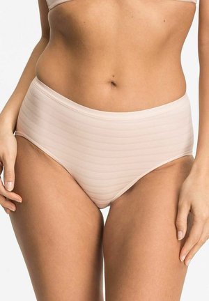 Frau trägt nahtlose, hellbeige, hochtaillierte Unterwäsche, die den Mittelteil und die Oberschenkel zeigt, vor einem weißen Hintergrund.