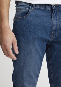 Jeans de denim azul oscuro con ajuste slim, que cuentan con bolsillos tradicionales y un sutil desgaste en la tela para dar textura.