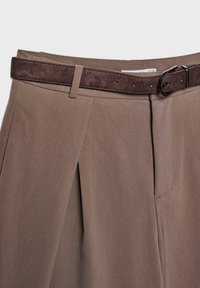 Rjave, krojene hlače s pregibi, narejene iz gladkega materiala. Imajo temno rjav usnjen pas z kovinsko zaponko.