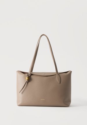 Grand sac cabas en cuir taupe avec longues poignées et petit détail de serrure dorée sur le côté, sur fond blanc uni.