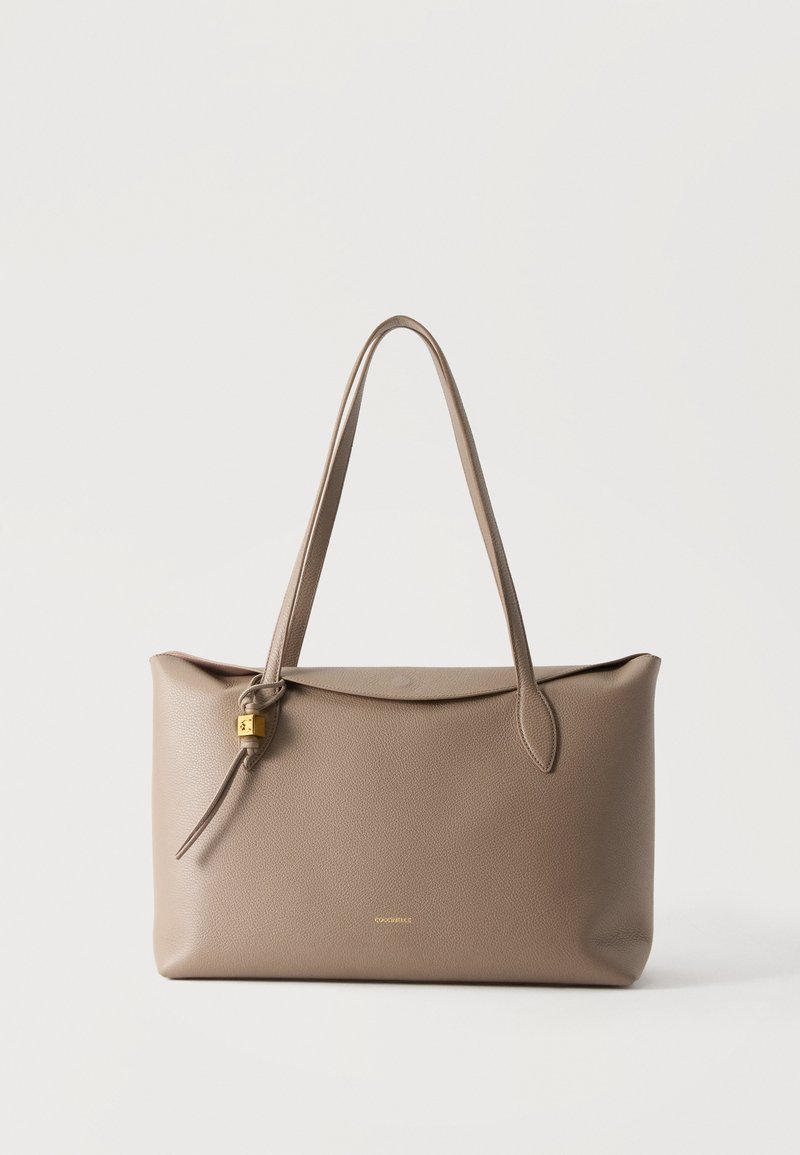 Grand sac cabas en cuir taupe avec longues poignées et petit détail de serrure dorée sur le côté, sur fond blanc uni.