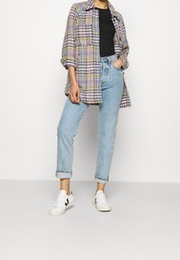 Camisa de cuadros en negro, rojo y amarillo, combinada con pantalones vaqueros claros enrollados y zapatillas blancas con detalles en negro.