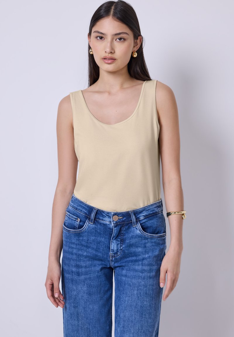 Beige top med scoop-neck, parret med højtaljede blå jeans. Stof udseendet er glat, og pasformen er afslappet.